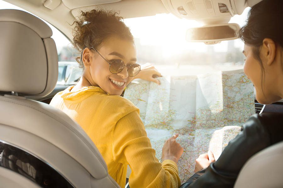 Personal Insurance - Happy Girlfriends Looking at a Map While Sitting in Their Car Before Taking a Road Trip